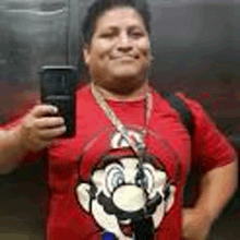 a man in a red shirt is taking a selfie in an elevator while wearing a mario shirt .