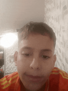 a young boy wearing an orange shirt with yellow stripes looks at the camera