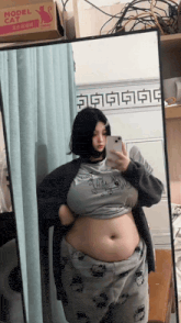 a woman is taking a picture of herself in front of a mirror with a model cat box in the background