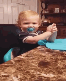 a baby with a pacifier in his mouth is sitting at a table in front of a sign that says washers