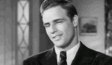 a man in a suit and tie is smiling and looking at the camera in a black and white photo .