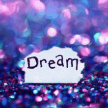 the word dream is written on a piece of paper on a glittery background .