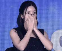 a woman is covering her face with her hands while sitting in front of a blue screen .