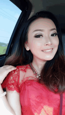 a woman wearing a red top and necklace is smiling