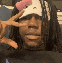 a man with dreadlocks is wearing a hello kitty hat and giving the peace sign .