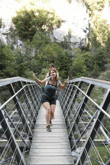 two women are walking across a bridge and one is giving a thumbs up