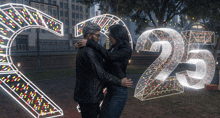 a man and a woman are hugging in front of a glowing number 25