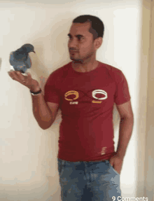 a man in a red shirt holds a pigeon on his finger