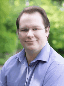 a man with glasses and a blue shirt smiles for the camera