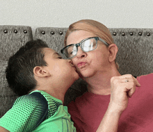 a woman wearing glasses kisses a young boy who is wearing a green shirt