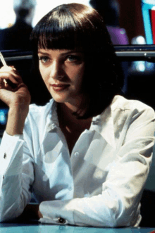 a woman in a white shirt is sitting at a table smoking a cigarette