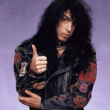 a man in a leather jacket with roses on the sleeves giving a thumbs up