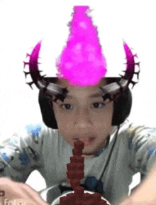 a young boy wearing a horned hat with a pink flame coming out of it is sitting at a table .