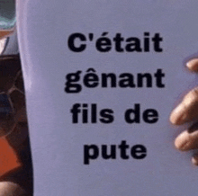 a person is holding a piece of paper with the words `` c 'était genant fils de pute '' written on it .