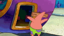 patrick star from spongebob squarepants is holding a wooden sign in front of a doorway .
