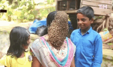 a boy and two girls are standing next to a woman with a bunch of bees on her head .