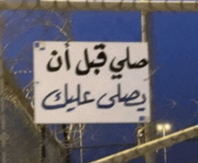 a sign with arabic writing on it hangs from a fence