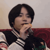 a man in a varsity jacket is singing into a microphone while sitting on a red couch