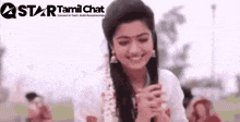 a woman is smiling with her hands folded and a star tamil chat logo in the background .