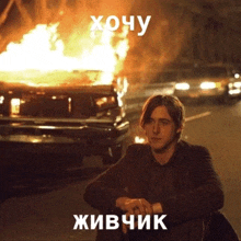 a man sits in front of a burning car with the words " хочу " on the top