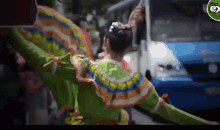 a woman in a colorful dress is dancing in front of a bus with the word ex on the corner