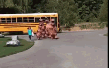 a group of people dressed in dinosaur costumes are walking down a street in front of a school bus .