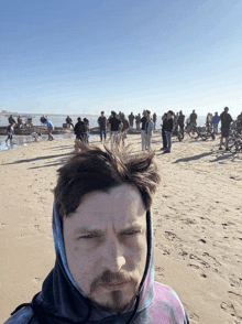 a man in a tie dye hoodie stands on a beach