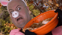 a man in a pig costume is holding an orange bowl of food