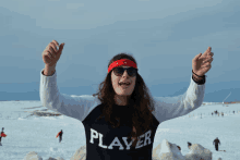 a woman wearing a player sweater stands in the snow with her arms outstretched