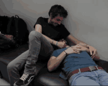 two men laying on a couch with one wearing a black shirt and the other a blue shirt