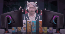 a man wearing headphones is sitting in front of two computer monitors with pringles chips .