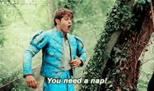 a man in a blue jacket says " you need a nap " in front of a tree