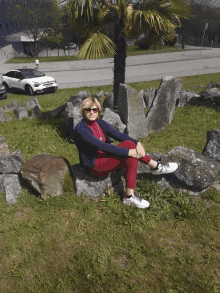 a woman sits on a rock in front of a palm tree and a white car