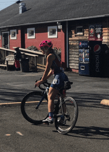 a woman riding a bike next to a pepsi machine