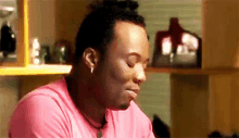 a man in a pink shirt is sitting at a table with his eyes closed .