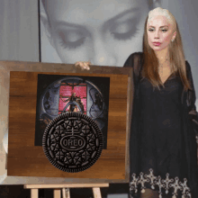 a woman in a black dress holds a framed picture of a oreo cookie