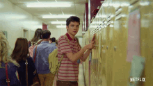 a man in a striped shirt is looking at a locker in a hallway with netflix written on the bottom