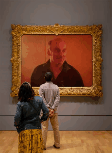 a man and a woman are looking at a framed painting of a man