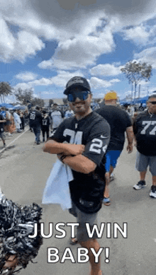 a man in a raiders jersey is standing in a crowd with his arms crossed and holding a towel .