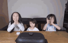 three little girls are sitting at a table with their hands on their faces in front of a sesame brand pan