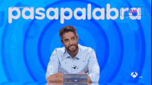 a man is laughing in front of a blue background that says pasapalabra