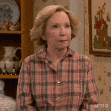 an older woman wearing a plaid shirt is sitting in front of a shelf with a picture of a basket on it