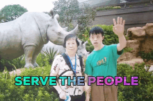 a man with down syndrome stands next to a woman in front of a rhino statue with the words serve the people written above them