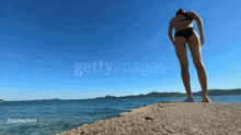 a woman in a black bikini is standing on a cliff overlooking the ocean with the watermark gettyimages on the bottom