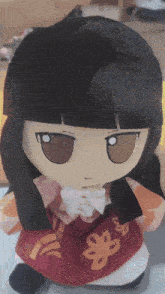 a stuffed doll with black hair and a red dress with a flower on it is sitting on a table
