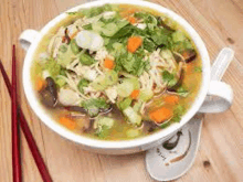 a bowl of soup with noodles and vegetables on a wooden table with chopsticks .