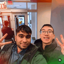 two men pose for a picture in front of a red exit sign