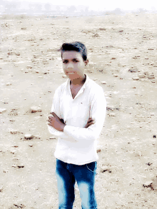 a young man in a white shirt and blue jeans stands in a desert with his arms crossed