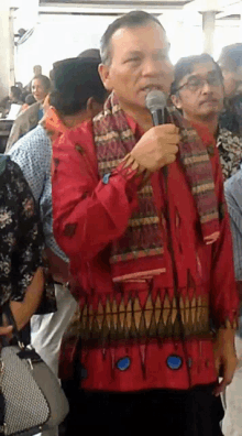 a man in a red shirt is holding a microphone in front of a crowd