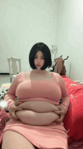 a woman in a pink dress is sitting on a bed with her hands on her stomach .